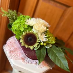Mixed bouquet with a sunflower, cream roses, and white blooms in a burgundy container