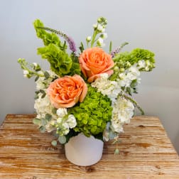 Peach roses and white flowers arranged in a white vase