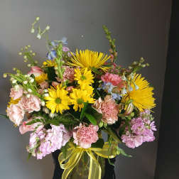 Mixed bouquet of yellow daisies and pink flowers in a glass vase with ribbon