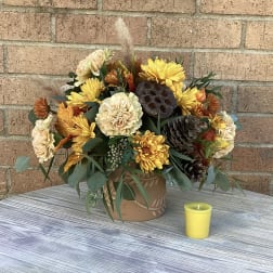 Autumn flower arrangement in a decorative pot with a small yellow candle nearby