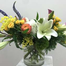 Mixed bouquet with white lilies, yellow roses, and purple spikes in a glass vase