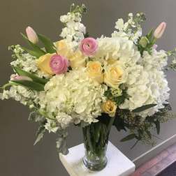 Bouquet of white hydrangeas, yellow roses, and pink tulips in a glass vase