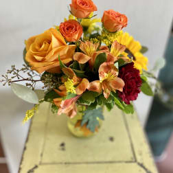 Bouquet of orange and yellow roses with mixed flowers in a glass vase