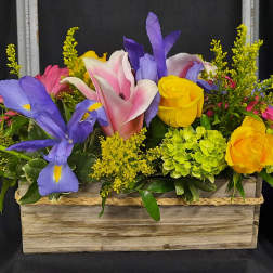 Colorful floral arrangement in a wooden box with yellow roses and purple irises