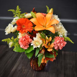 Orange lilies and mixed flowers arranged in an amber glass vase.