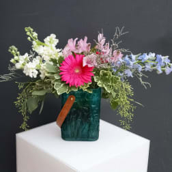 Mixed bouquet in a teal glass vase with a leather strap