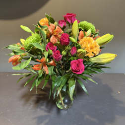 Mixed bouquet of pink roses, orange alstroemeria, and yellow blooms in a glass vase