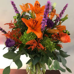 Orange lilies and purple flowers in a glass vase