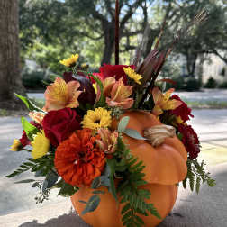 Fall floral arrangement in a carved pumpkin with red, orange, and yellow blooms