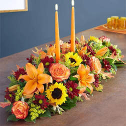 Low floral centerpiece with orange lilies, roses, sunflowers, and two orange taper candles