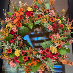 Autumn wreath with orange, red, and yellow flowers on a dark door