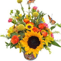 Sunflower and orange rose arrangement in a decorative vase with butterfly picks