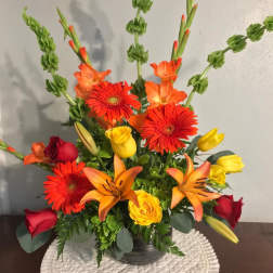 Mixed bouquet with red and yellow roses, orange lilies, and gerbera daisies in a vase