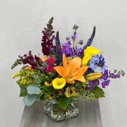Colorful mixed bouquet in a clear glass vase with lilies, calla lilies, and snapdragons