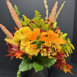 Orange lilies and yellow roses in a dark vase with autumn foliage