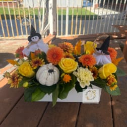 Halloween floral arrangement with yellow roses, orange blooms, and small witch decorations