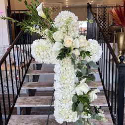 White floral cross arrangement on an easel with roses and calla lilies