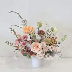 Asymmetrical arrangement of peach and blush flowers in a white cylinder vase
