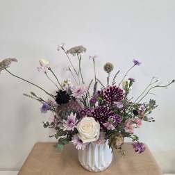 Mixed purple and white floral arrangement in a white vase