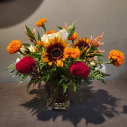 Mixed bouquet of sunflowers, white roses, and orange marigolds in a glass vase