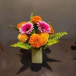 Pink gerbera daisies and orange marigolds in a small vase