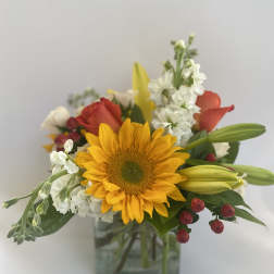 Mixed bouquet with a sunflower, lilies, roses, and white blooms in a glass vase