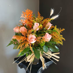 Pink roses in a glass vase with orange filler and dried grass accents