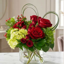 Red roses and green hydrangeas in a clear glass vase with heart-shaped loops