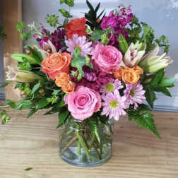 Mixed bouquet of pink, peach, and purple flowers in a glass vase