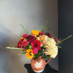 Mixed bouquet in a brown ceramic pitcher with yellow, pink, red, and cream blooms