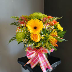 Bright mixed bouquet in a glass vase with a pink plaid ribbon
