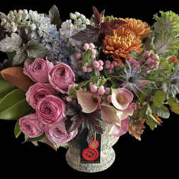Lush arrangement with pink roses, mini calla lilies, orange mums, blue flowers and ornamental cabbage in a footed vase