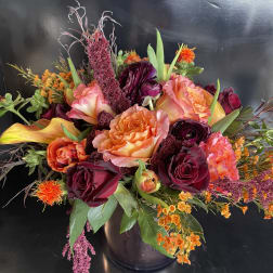 Mixed bouquet of roses, calla lilies, and orange accent flowers in a dark vase