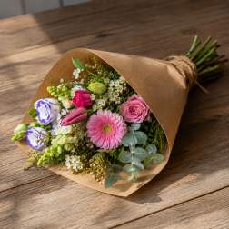 Hand-tied bouquet of pink, white, and purple flowers in brown paper