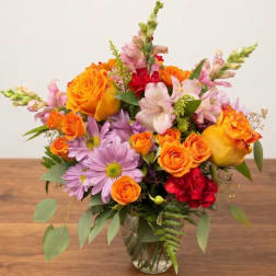 Mixed bouquet of orange roses, pink lilies, and purple daisies in a glass vase