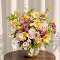 Pastel mixed flower arrangement in a round vase on a table