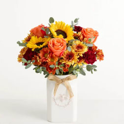 Bouquet of sunflowers, roses, and mums in a white vase with a ribbon