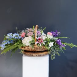 Basket arrangement of mixed pastel flowers with a wicker handle