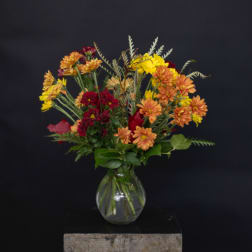 Mixed bouquet of orange, yellow, and red flowers in a clear glass vase