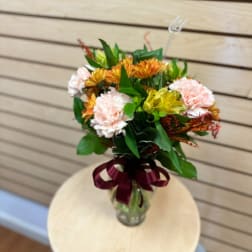 Bouquet of peach carnations and orange flowers in a glass vase with a ribbon