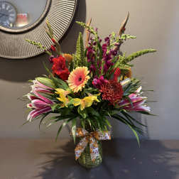 Colorful mixed flower arrangement in a glass vase with a patterned ribbon