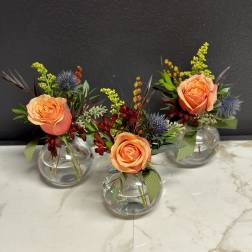 Three small floral arrangements in round glass vases with peach roses