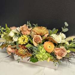 Low floral arrangement with peach roses, white blooms, and yellow chrysanthemums in a white box.