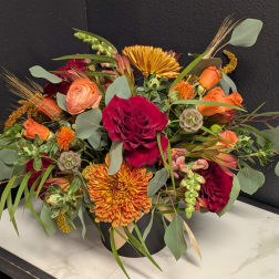 Mixed bouquet of red, orange, and peach flowers in a black vase