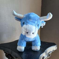Blue plush bull toy with silver horns standing on a dark shelf