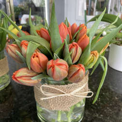 Orange tulip bouquet in a glass vase wrapped with burlap and ribbon