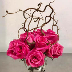 Hot pink roses arranged in a clear glass vase with curly branches