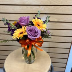 Bouquet of purple roses and yellow gerbera daisies in a glass vase