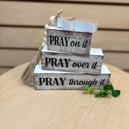 Stacked wooden blocks with prayer phrases and a tassel on a tabletop