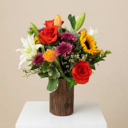 Mixed bouquet of roses, lilies, sunflowers, and mums in a wooden vase